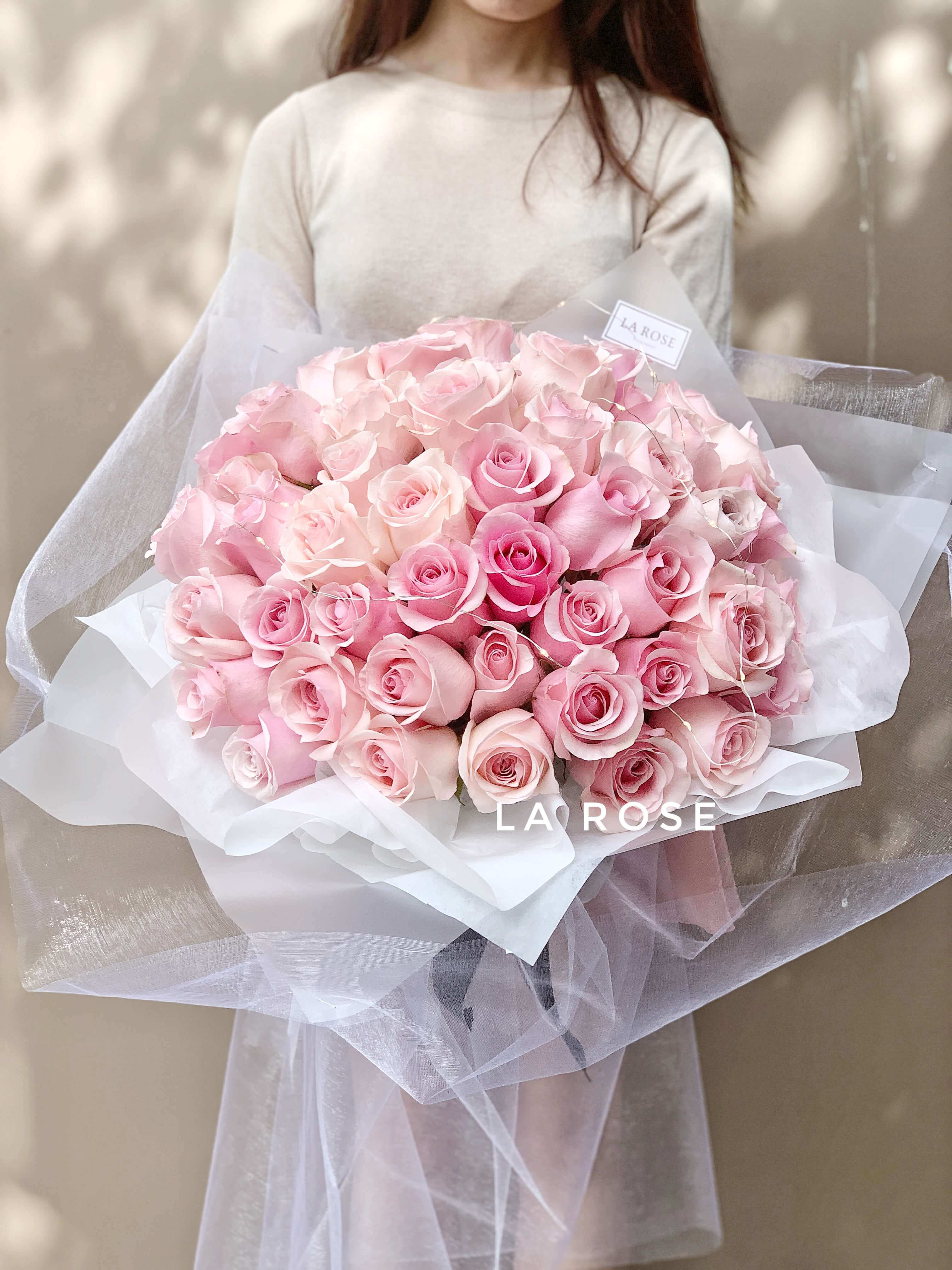 A girl holding a large La Rose Fleur bouquet with 51 pink flowers